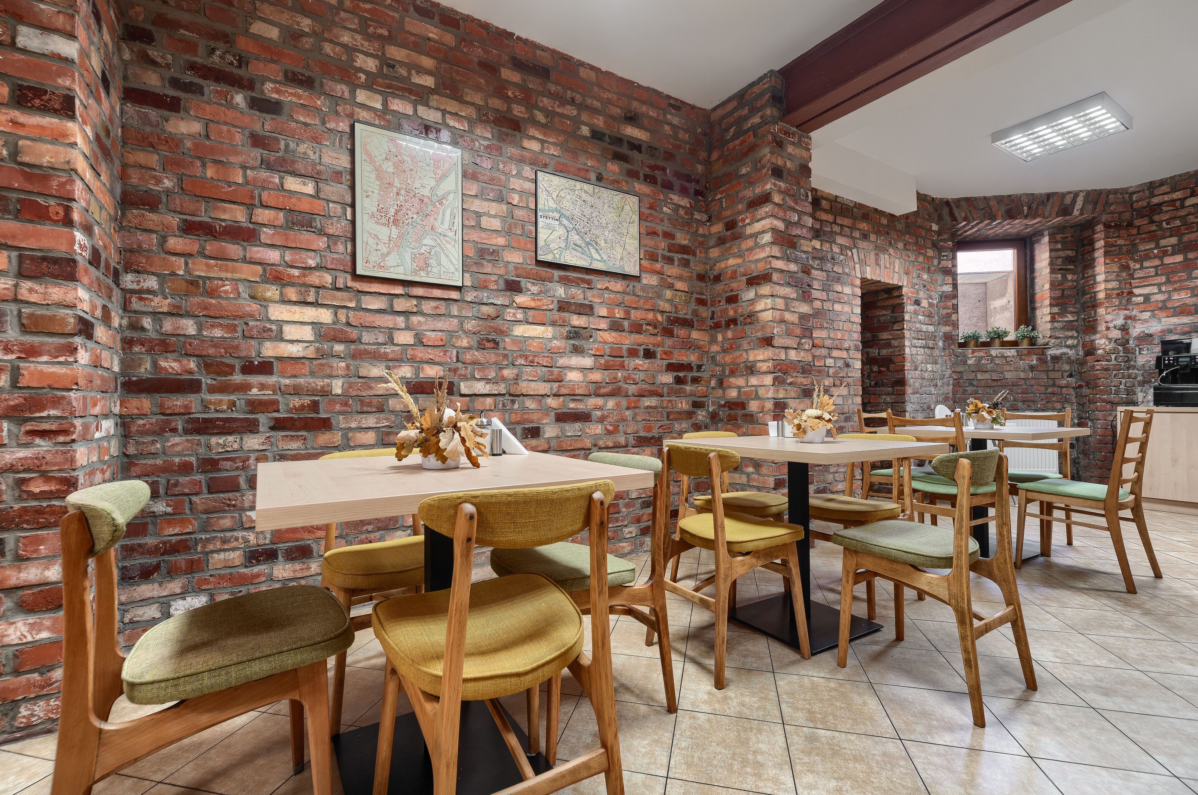 Comedor con paredes de ladrillo, mesas y sillas de madera, y dos mapas enmarcados en la pared.