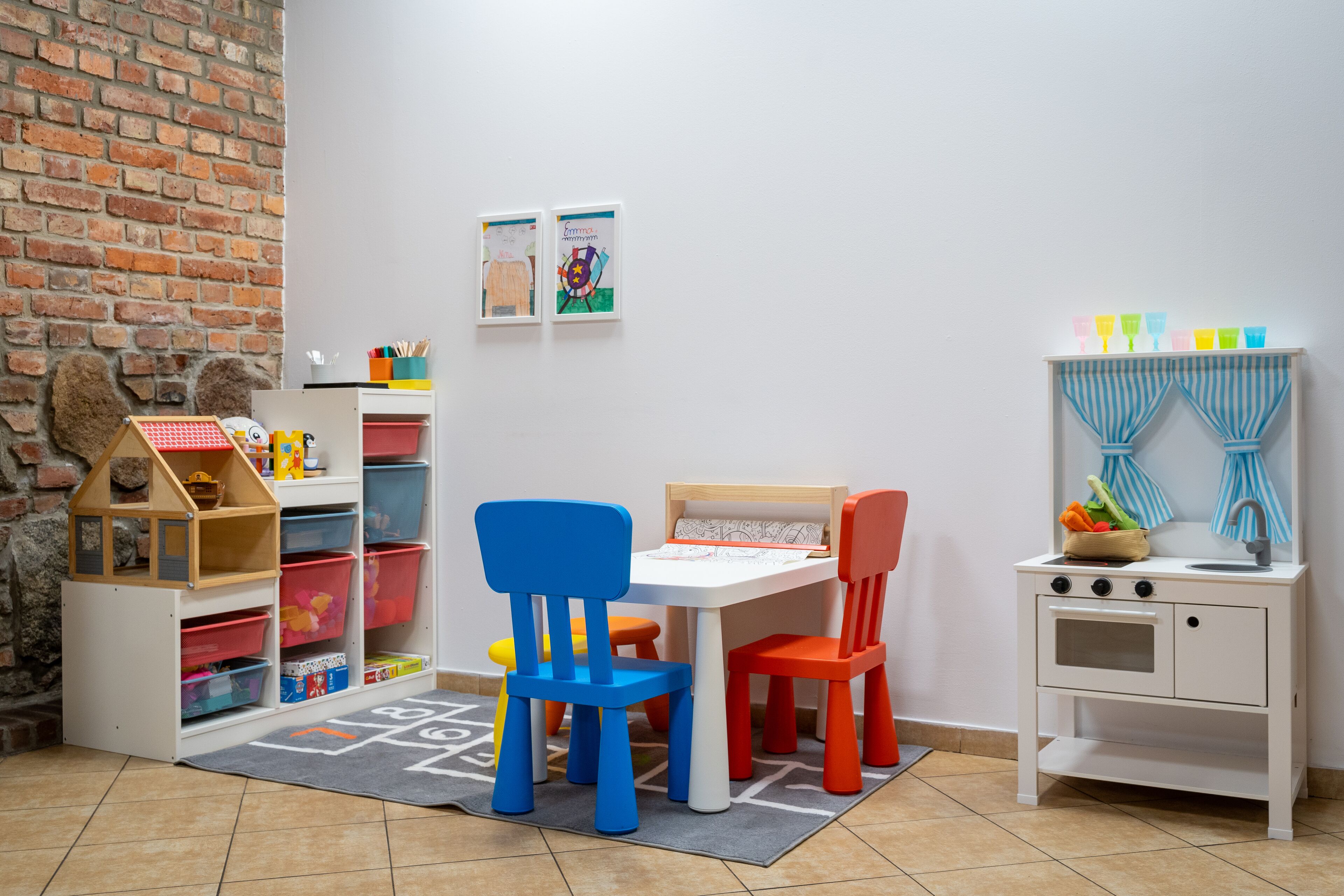 Una sala de juegos con pared de ladrillo, una casita de juegos y una cocina de juguete.