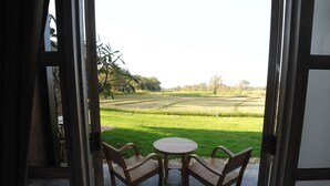 An open door leading to a patio with a round table and two wooden chairs, overlooking a green field. - Nansripanna Resort (Nan)