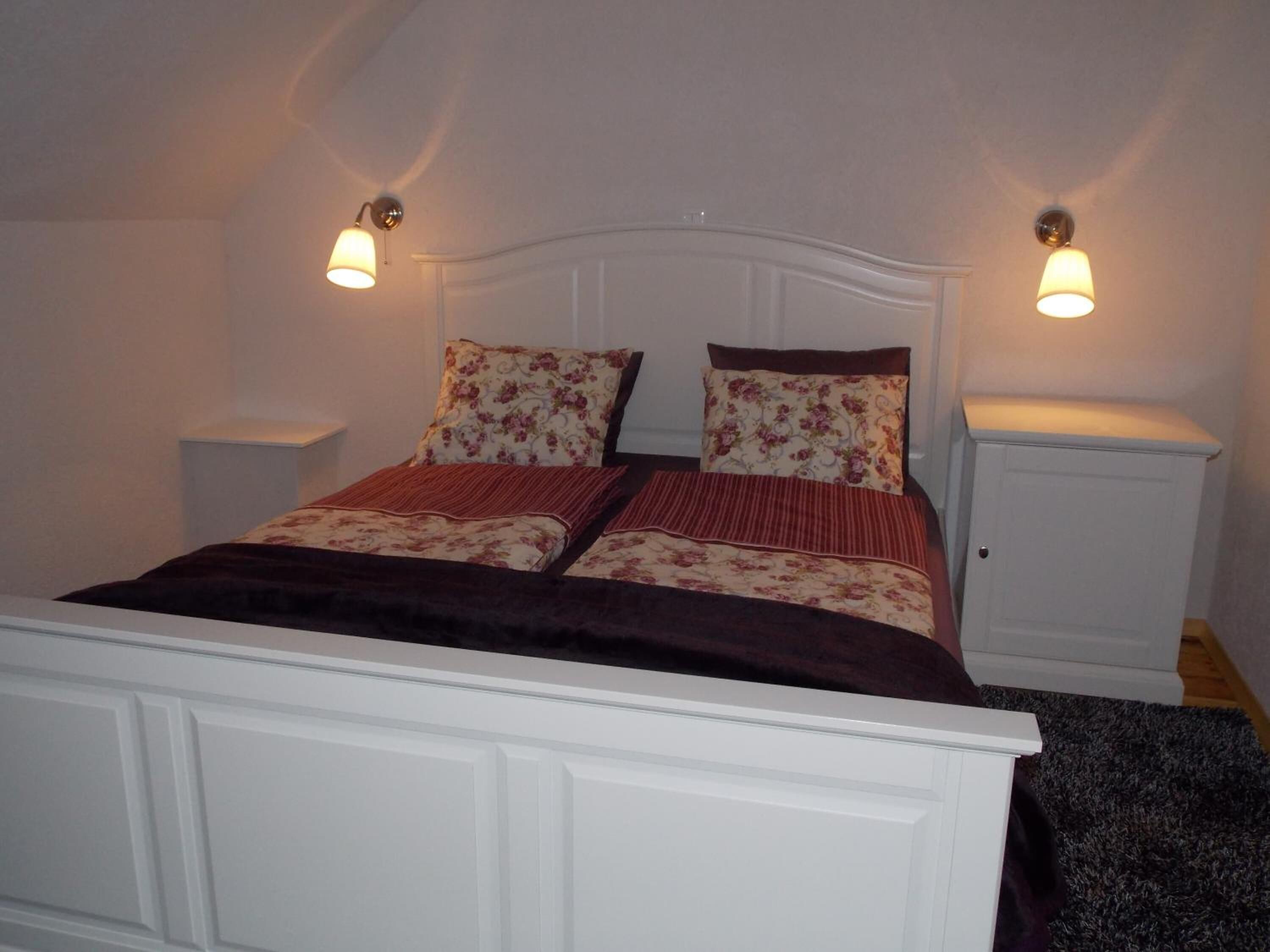 A neatly made bed with floral bedding and two bedside lamps.
