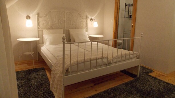 Une chambre à coucher avec un lit en métal blanc, deux tables de chevet et un miroir au mur.