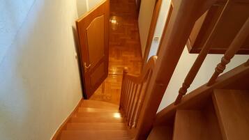 Una escalera de madera con barandilla y una puerta al final que da a un cuarto con piso de madera.
