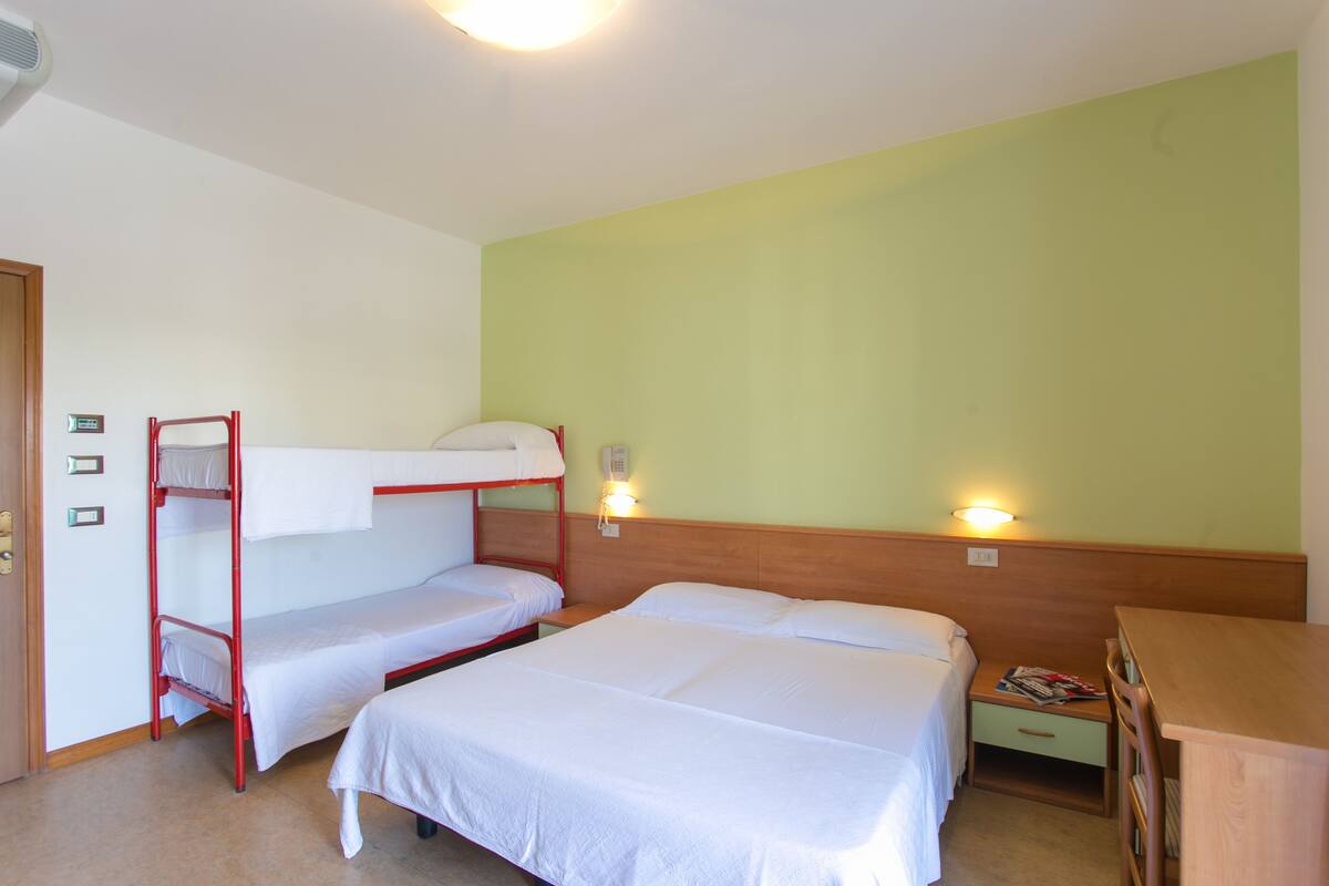 A room with bunk beds, a wooden desk, and two bedside lamps.