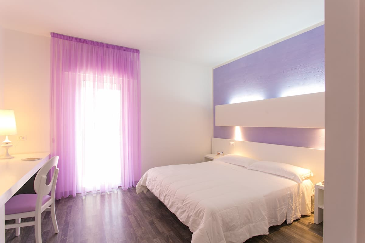 A bedroom with a bed, bedside table, lamp, chair, and a window with curtains.