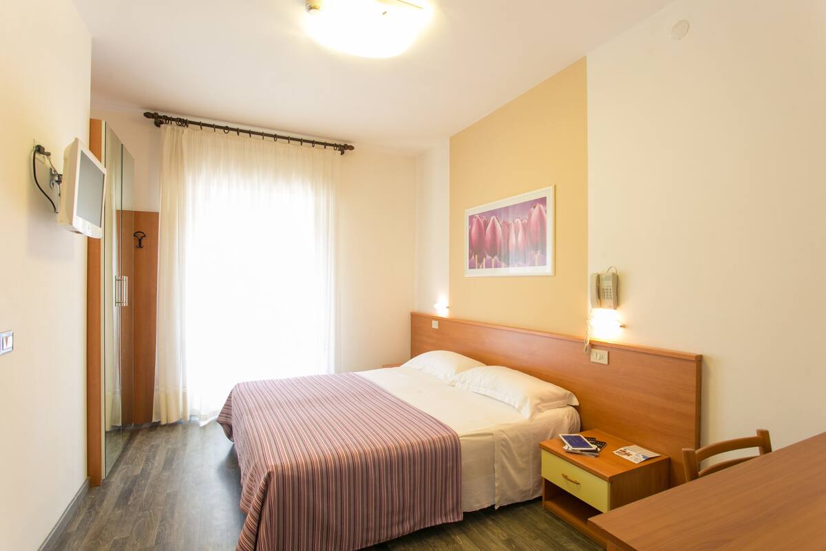 A hotel room with a bed, bedside table, and a desk.