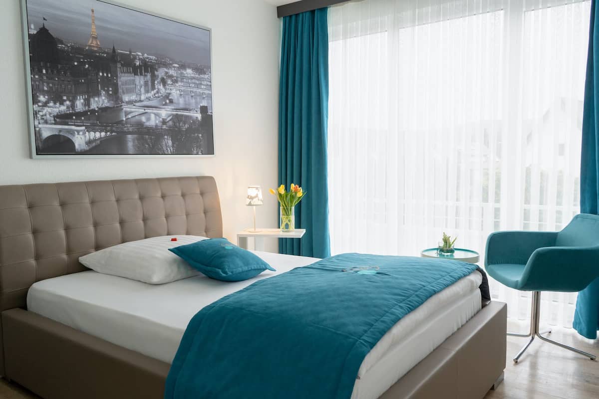 Ein Schlafzimmer mit einem Bett, einem Nachttisch, einer Lampe, einer Vase mit Blumen und einem Stuhl.