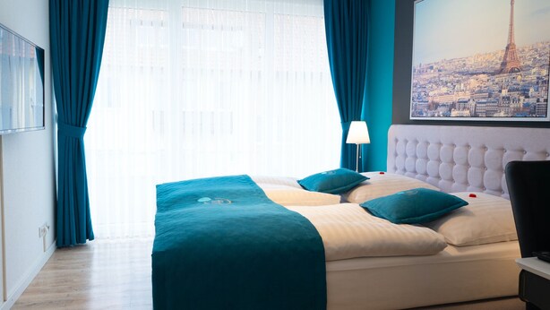 Une chambre d’hôtel avec un lit, une table de chevet, une lampe et une grande fenêtre avec des rideaux.
