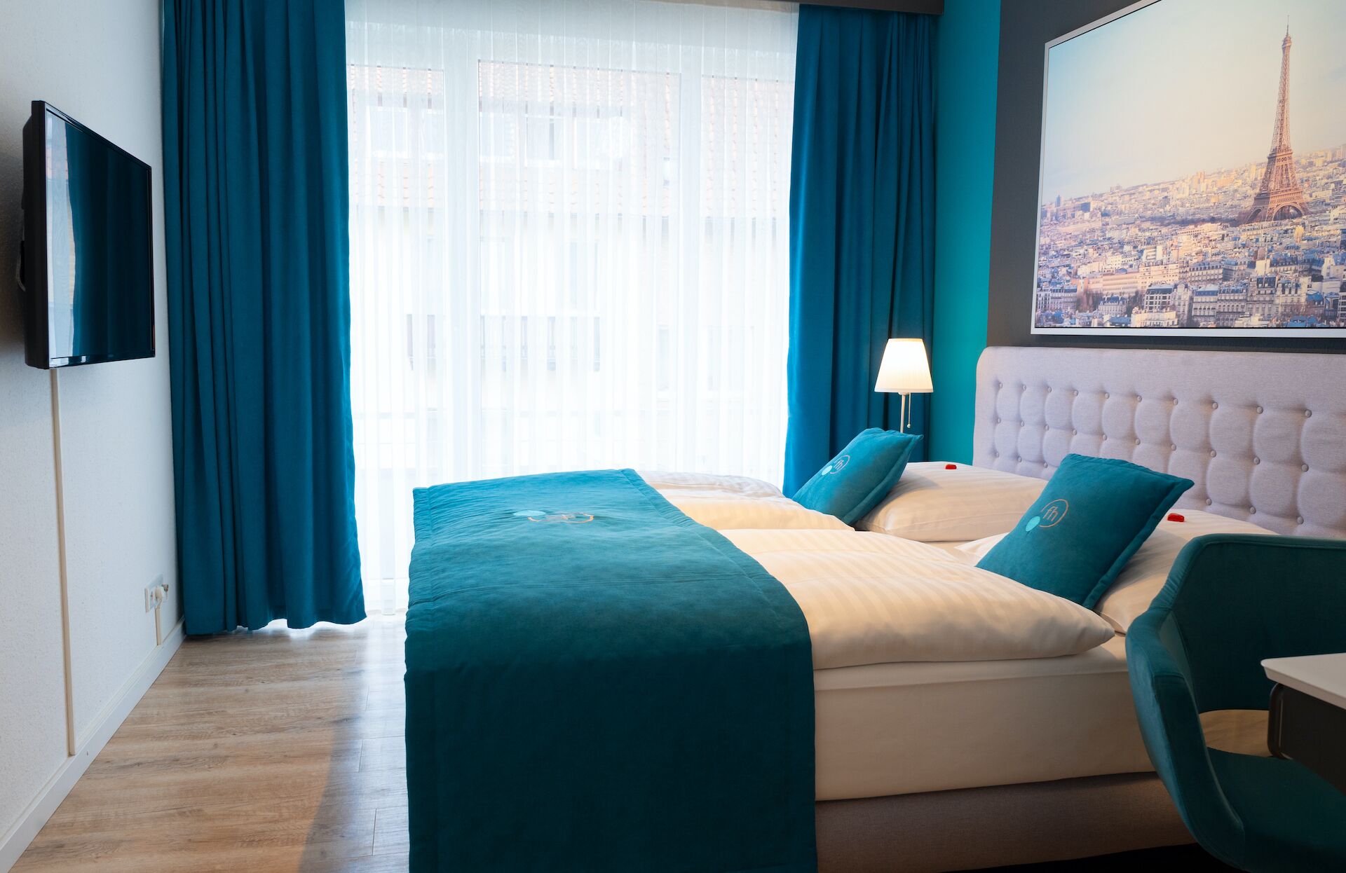 Habitación de hotel con cama, televisión, lámpara y un cuadro de la Torre Eiffel.
