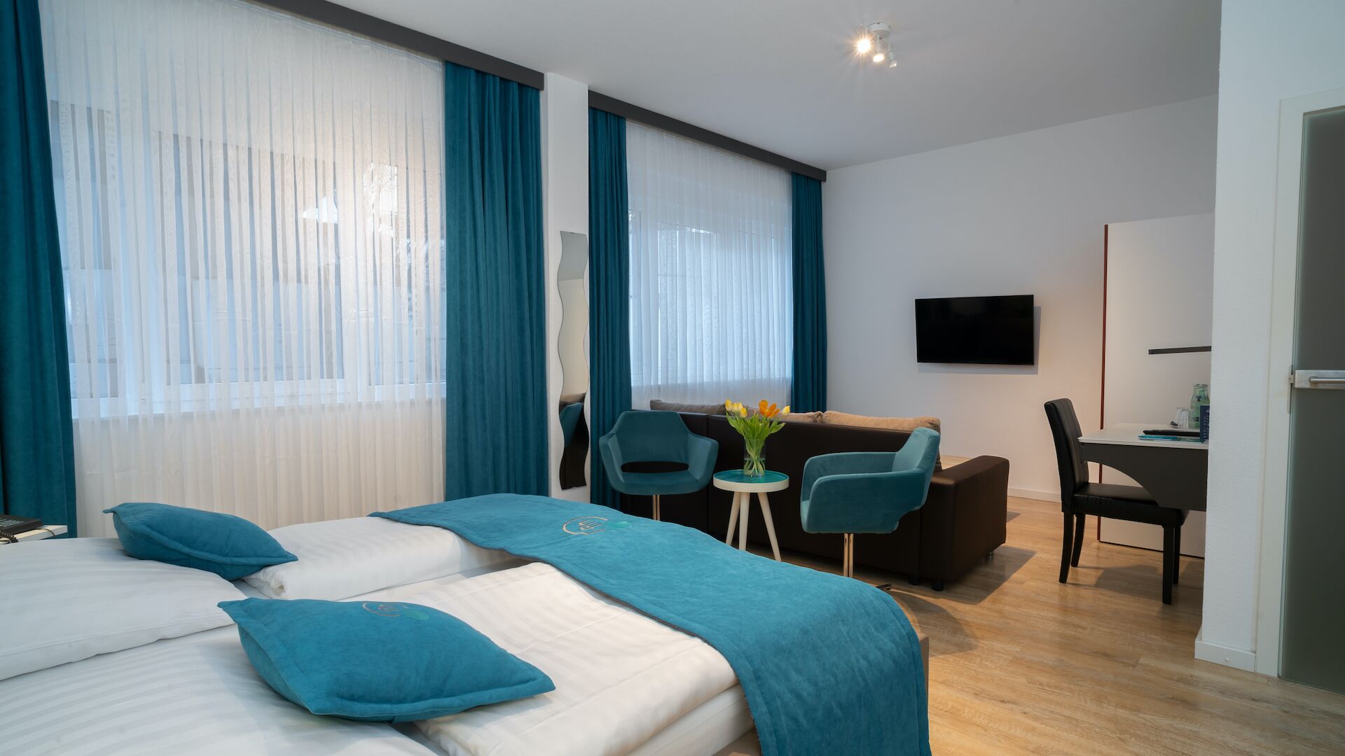 A hotel room with two beds, a desk, a chair, a TV, and a small table with a vase of flowers.
