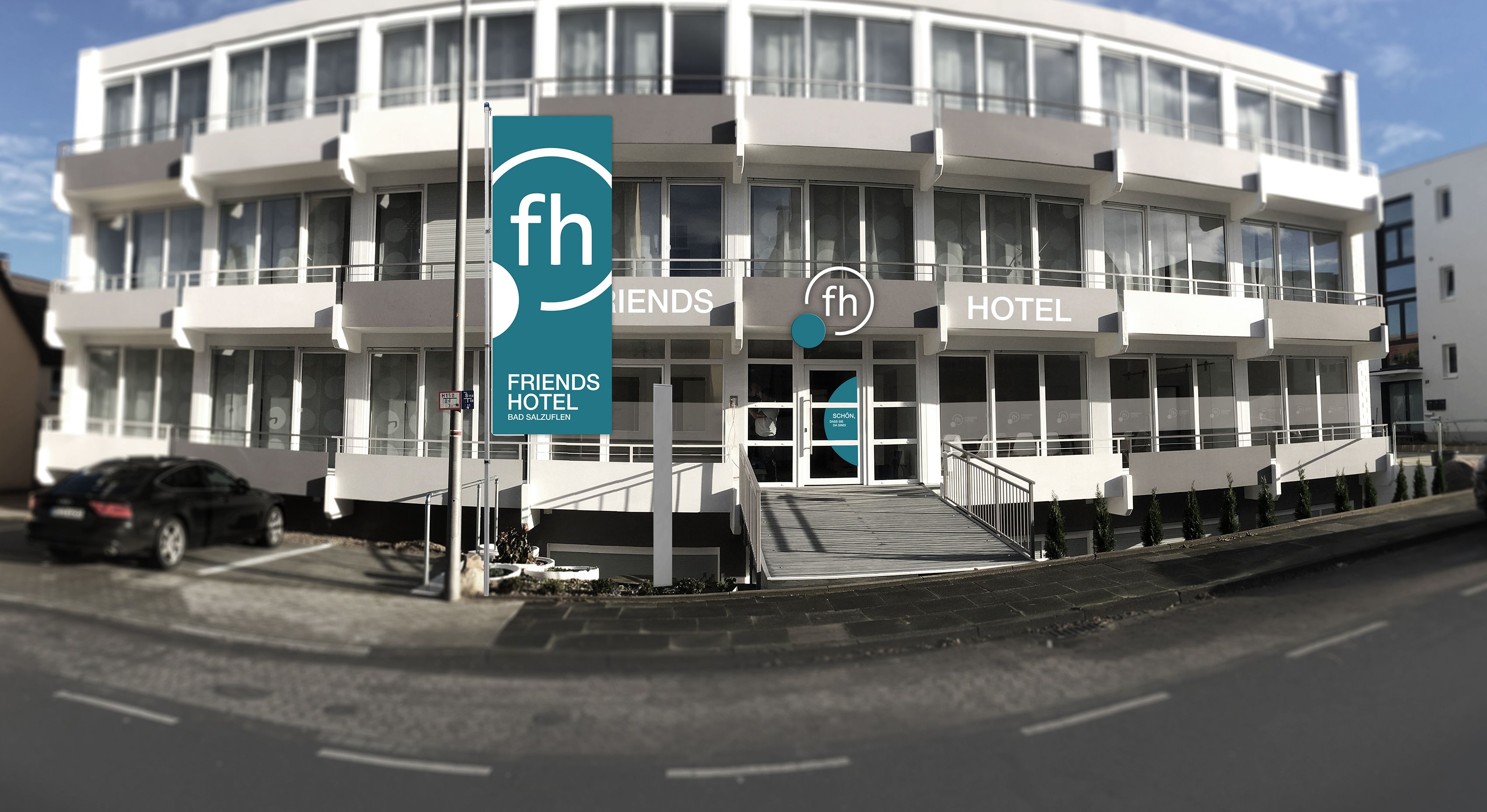 A modern building with a Friends Hotel sign, featuring a central entrance with a ramp, multiple balconies, and large windows.