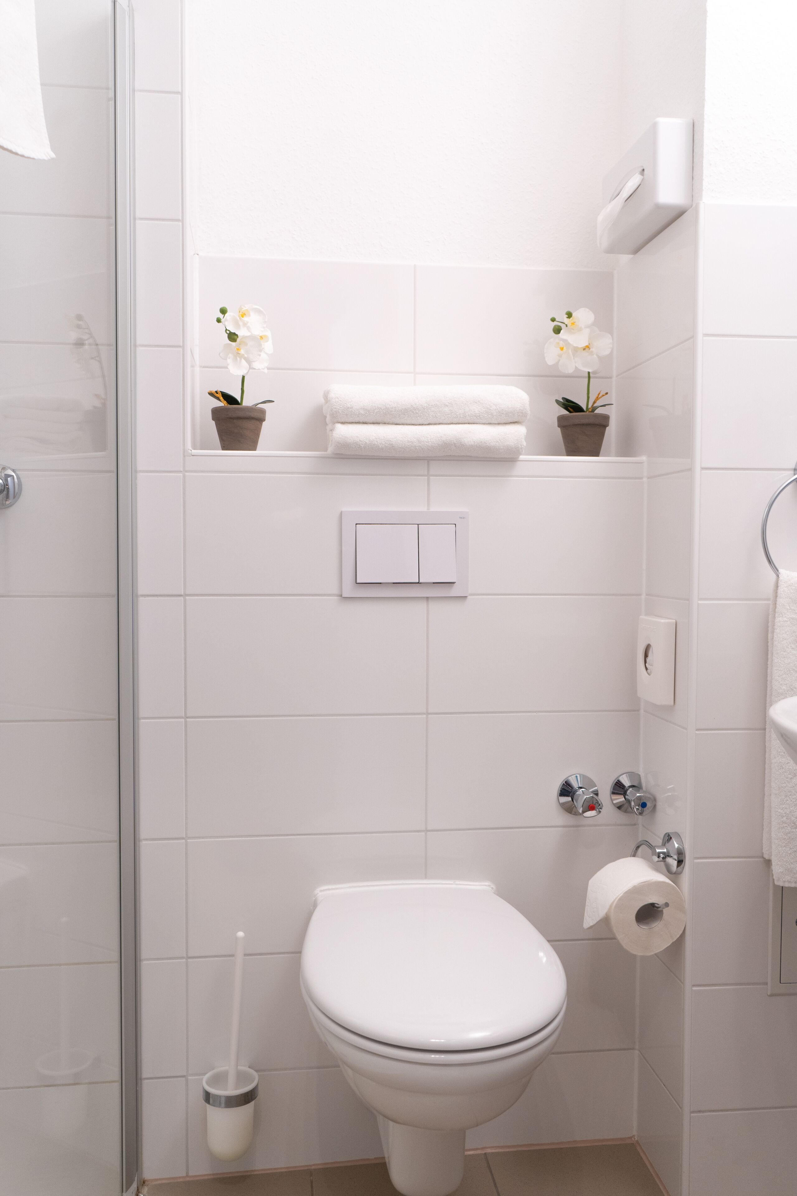 Un baño con inodoro, bidé, toallero y dos orquídeas en macetas.
