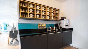 Une cuisine moderne avec un plan de travail noir, une machine à café et une étagère où sont rangées des tasses et des verres.