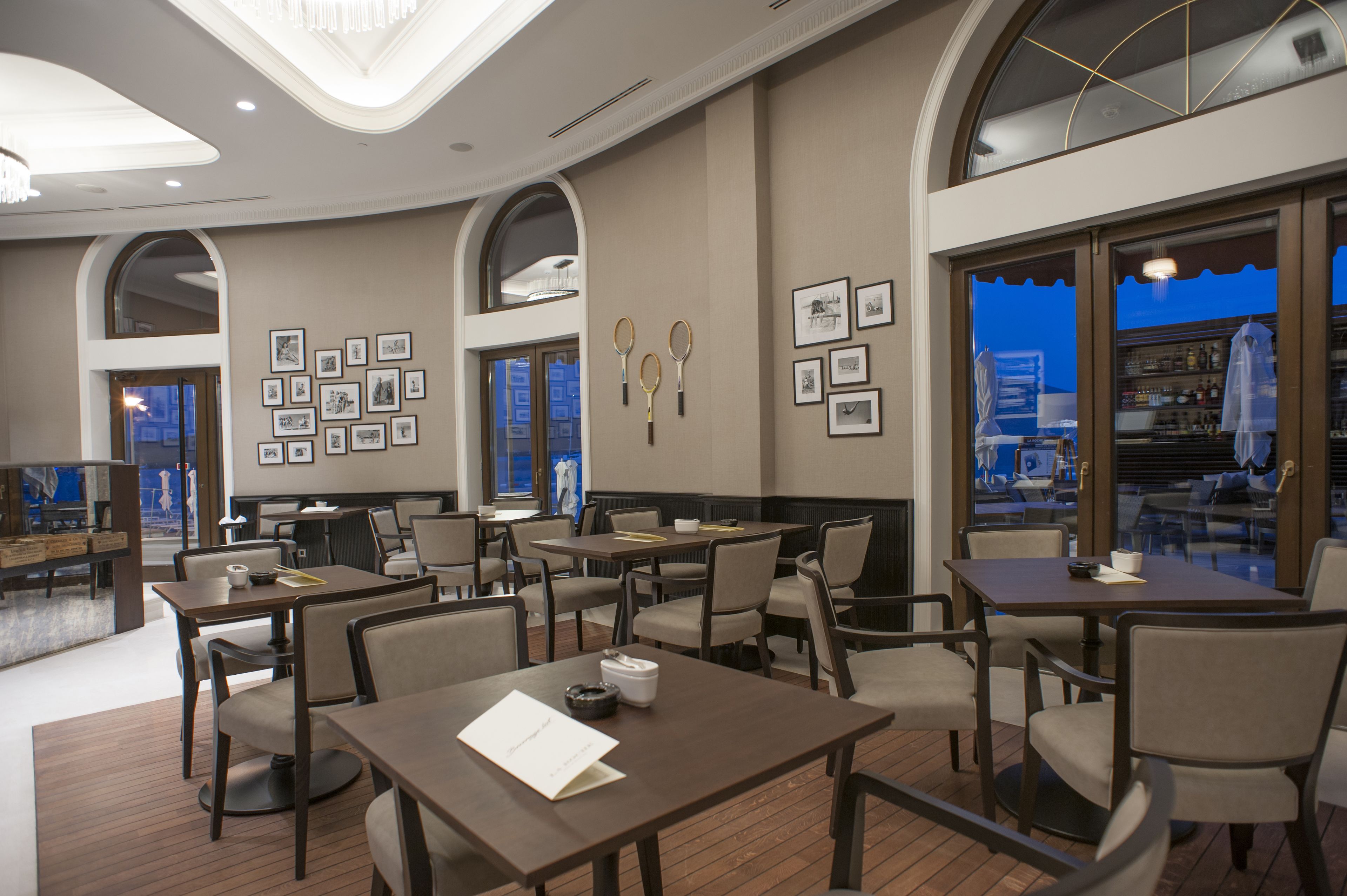 Comedor de hotel con varias mesas y sillas, cuadros en las paredes y vistas a través de las ventanas.