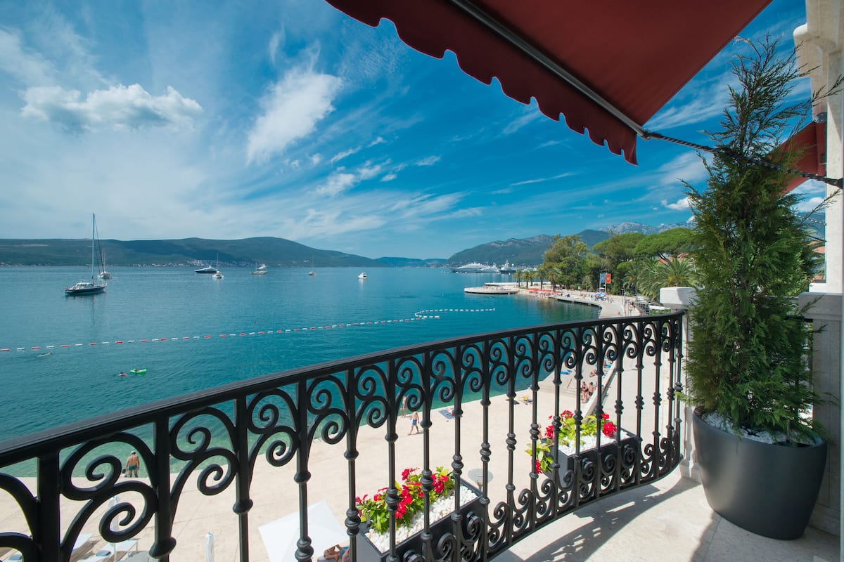 A balcony with a view of a calm sea, boats, and distant mountains.