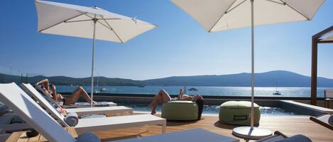 A poolside area with lounge chairs, umbrellas, and a view of the sea.