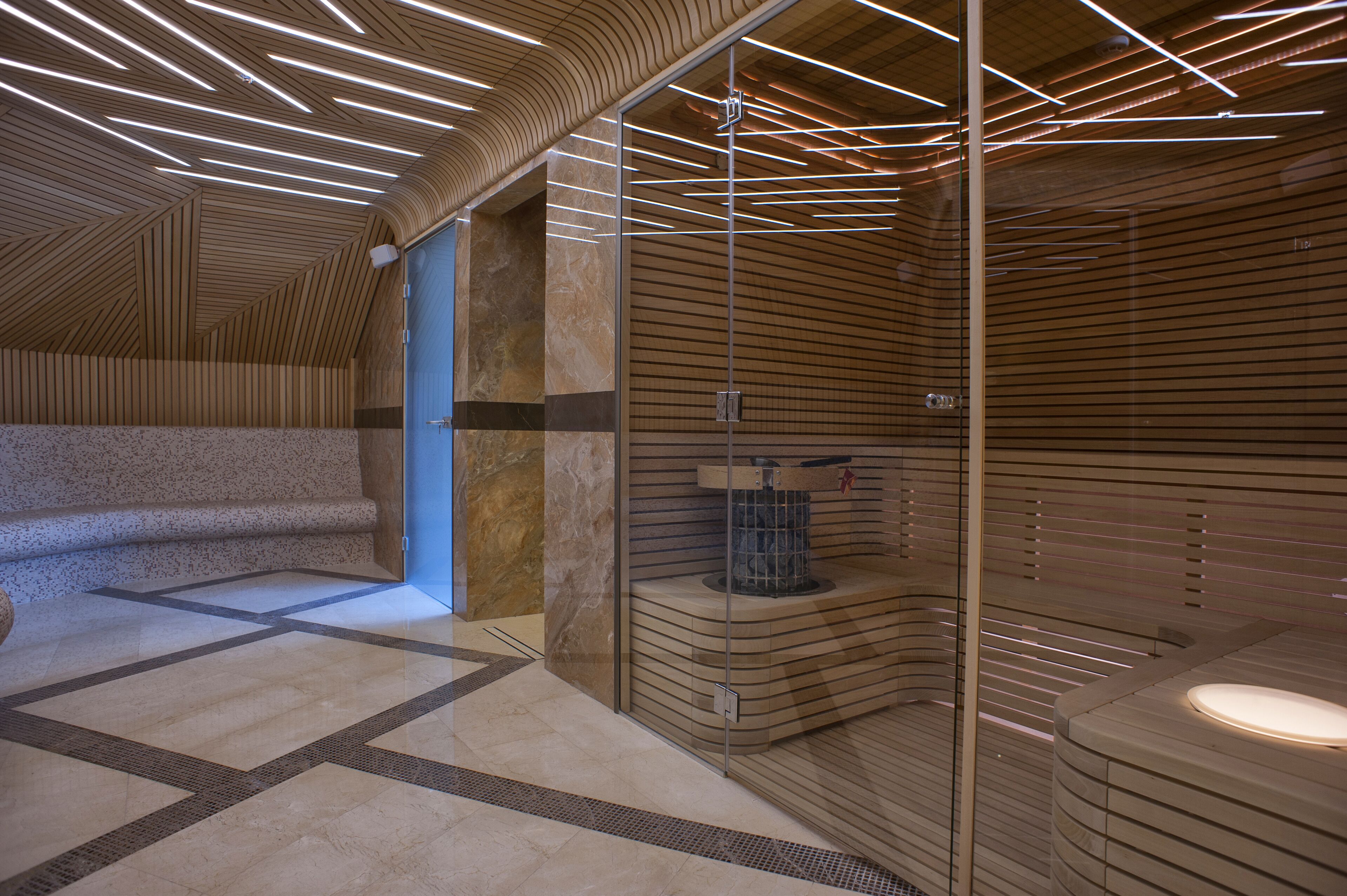 A modern spa area with a wooden ceiling, a glass partition, and a marble floor.