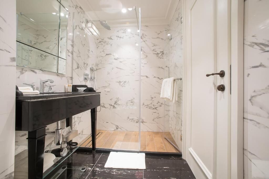 A modern bathroom with a glass-enclosed shower, a black sink, and a marble-tiled shower area.