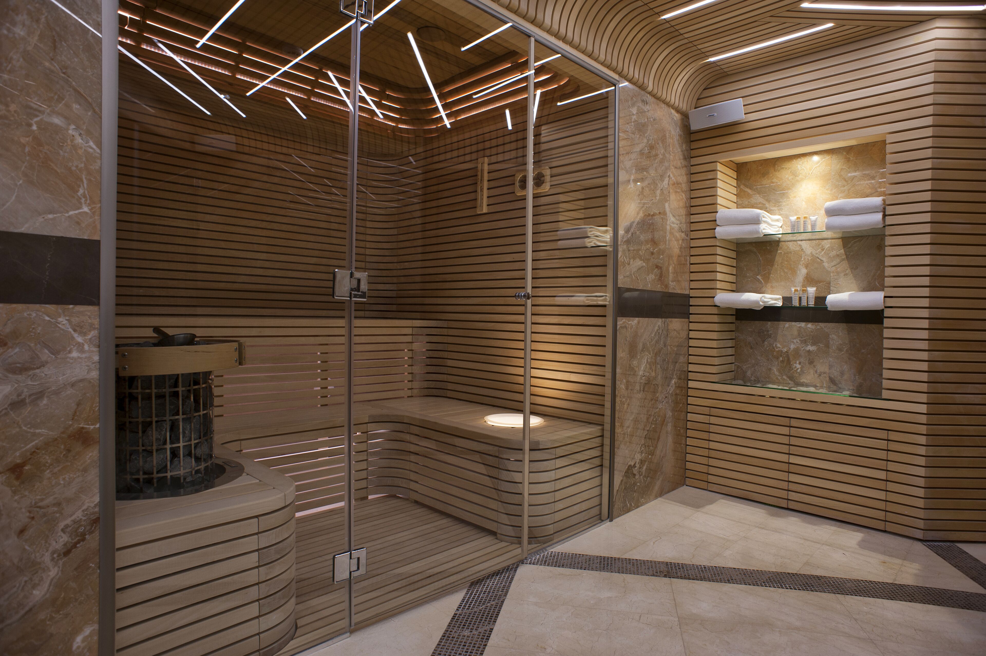Un spa moderno con una pared curva de madera, una ducha con cerramiento de vidrio y un suelo de baldosas de mármol.