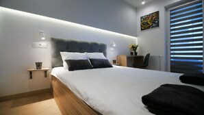 A modern bedroom with a large bed, bedside tables, a desk, and a window with blinds. - 4UApart - Apartment suite Picasso (Swinoujscie)