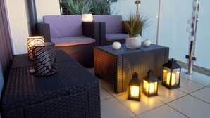 An outdoor seating area with wicker furniture, a cushioned sofa, and a small table with a potted plant. - 4UApart - Apartment suite Picasso (Swinoujscie)