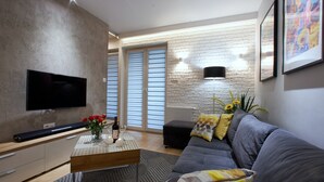 A modern living room with a flat-screen TV, a coffee table with decorative items, a sofa with patterned cushions, and a brick-patterned wall. - 4UApart - Apartment suite Picasso (Swinoujscie)