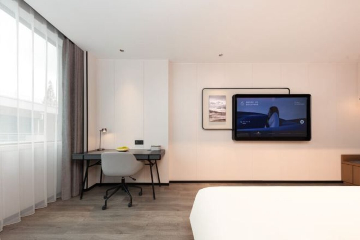 Une chambre d’hôtel moderne, dotée d’un grand lit, d’un bureau et d’un téléviseur à écran plat fixé au mur.