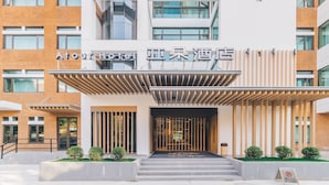 Entrada de un hotel con diseño moderno, destacando un frente de ladrillo, un área de acceso cubierta y un cartel con el nombre del hotel.