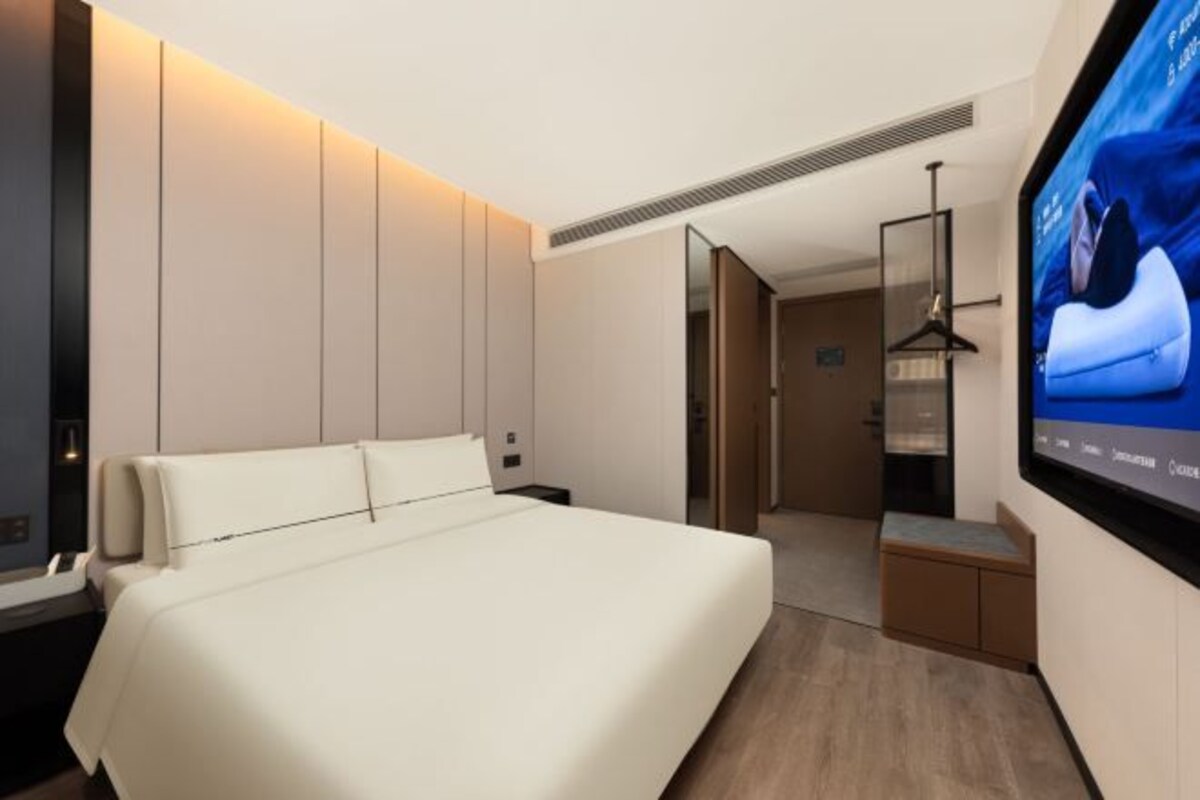 Une chambre d’hôtel moderne dotée d’un grand lit, d’un téléviseur à écran plat fixé au mur et d’un dressing.