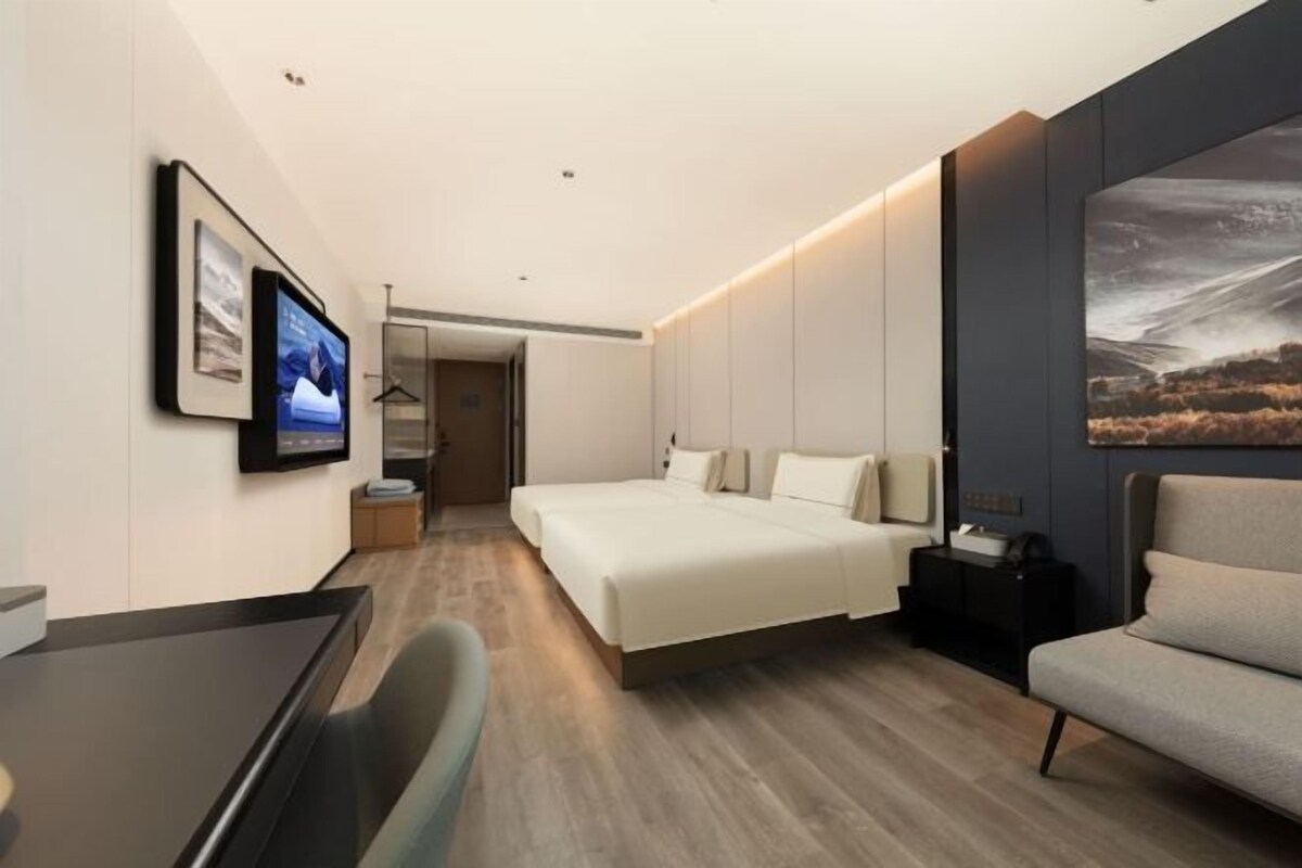 A modern hotel room with a large bed, a desk, and a TV mounted on the wall.