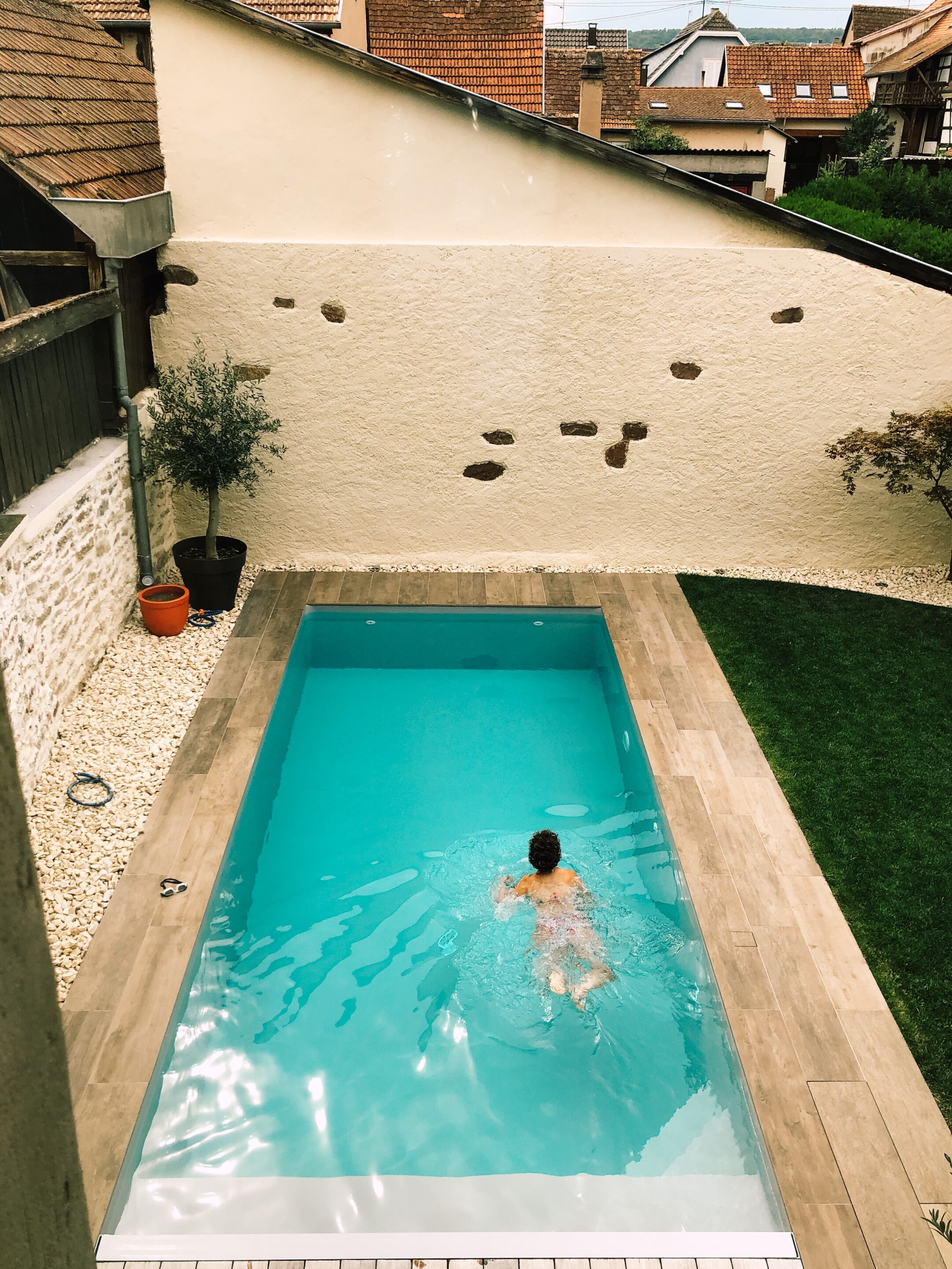 A rectangular swimming pool with clear blue water, surrounded by a pebble border and a tiled deck.