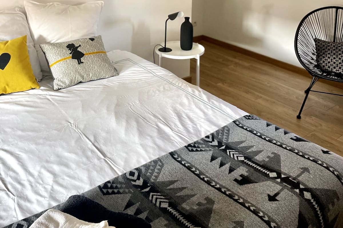 A modern bedroom with a large bed, a side table, a chair, and a large window.