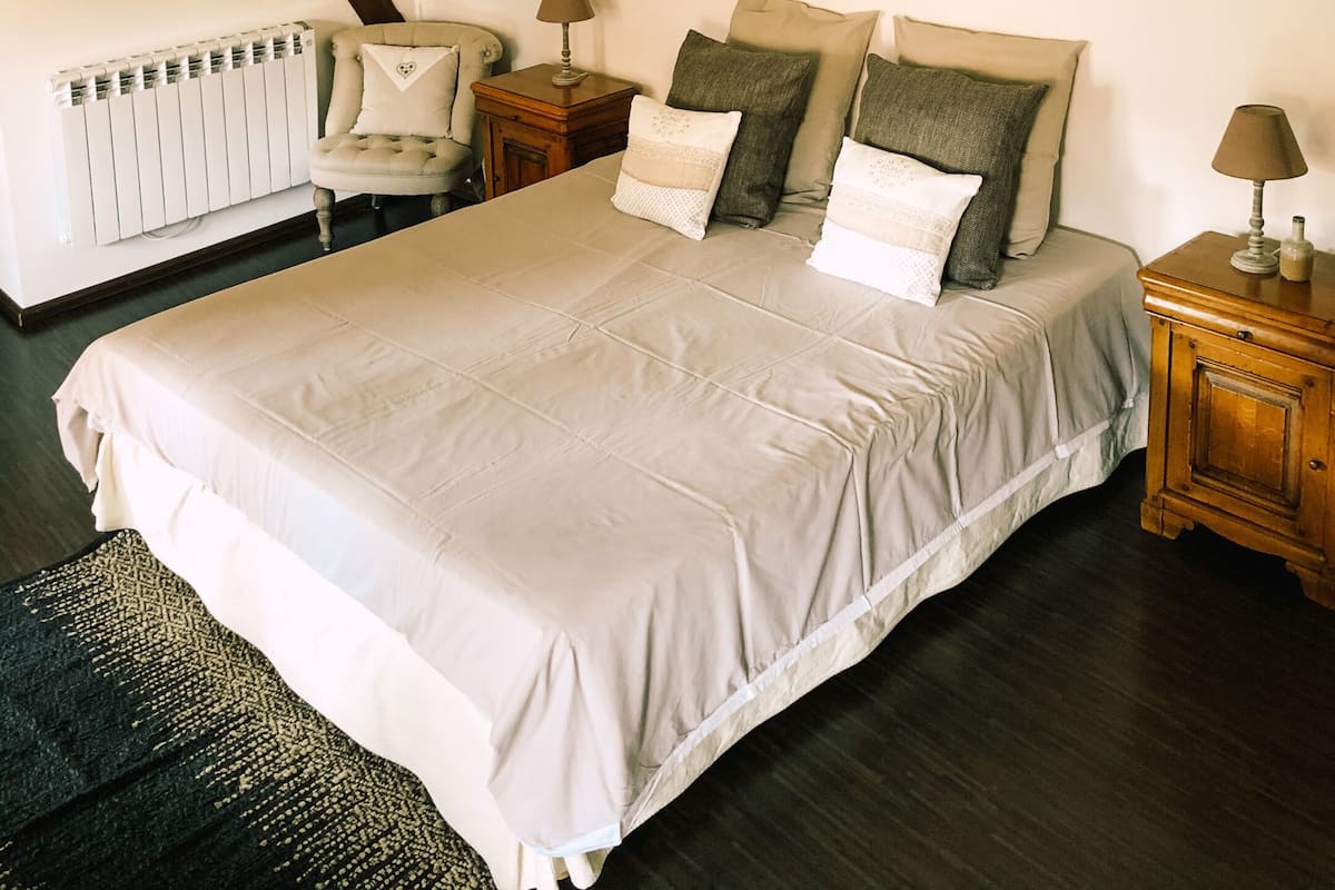 A bedroom with a large bed, two bedside tables, a radiator, and a sloped ceiling.