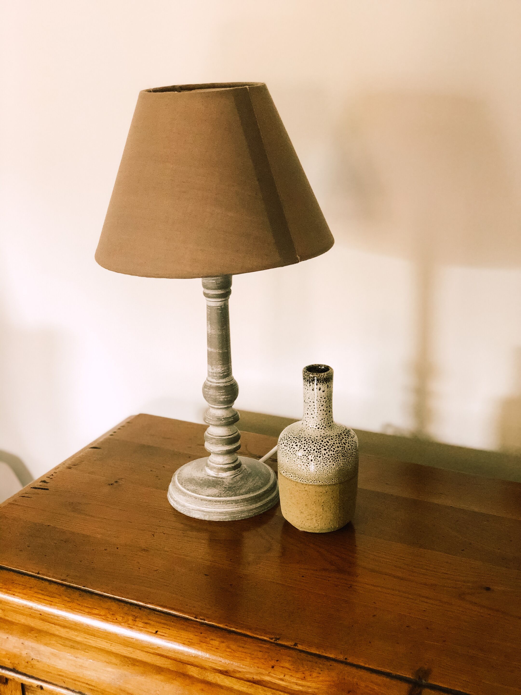 Een lamp met een kegelvormige kap en een keramieken vaas op een houten tafel.