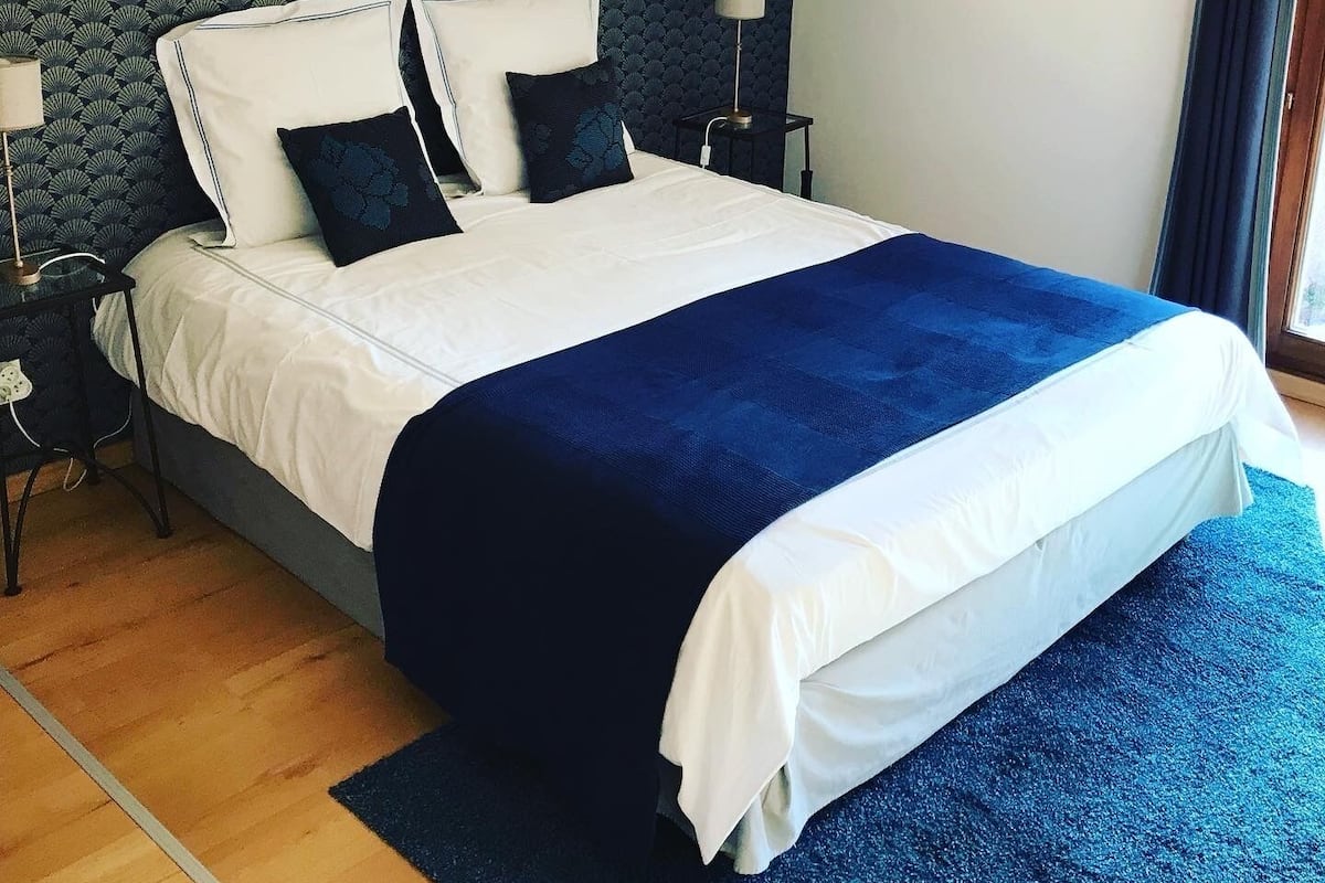 A neatly made bed with white and blue bedding, a dark headboard, and a small bedside table with a lamp.