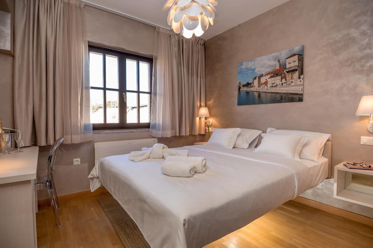 A modern hotel room with a large bed, a desk, and a window with curtains.