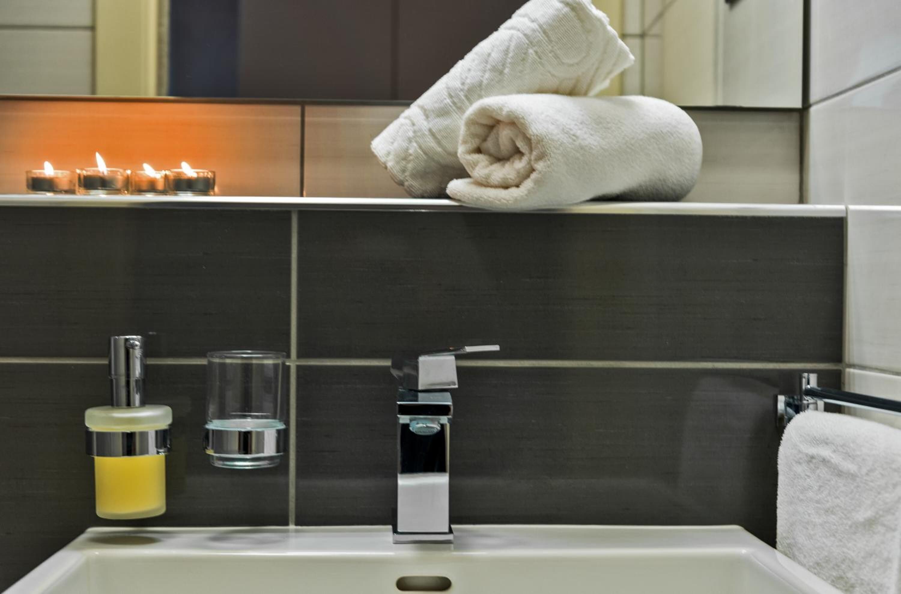 A modern bathroom with a bathtub, a towel rack, a soap dispenser, and a glass of water.