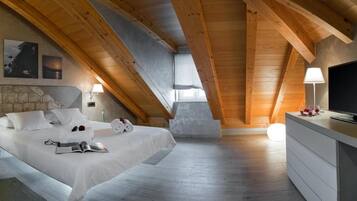 A bedroom with a sloped ceiling, a bed with white linens, a stone wall, a television, and a dresser.