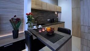 A modern kitchen with wooden cabinets, a black countertop, and a dining area with a table and chairs. - 4UApart - Apartment studio Platan New York (Swinoujscie)