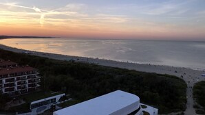 A coastal view with a beach, a modern building, and a distant shoreline. - 4UApart - Apartment studio Platan New York (Swinoujscie)