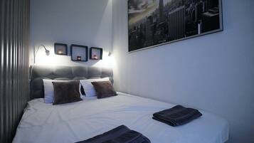Una cama bien hecha con almohadas, una toalla doblada y un cuadro con una vista urbana en la pared.