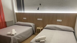 A hotel room with two beds, each with a quilted bedspread and a rolled towel. There is a small round table between the beds, and a window with a view of the outside. - Hostal Uria (Salamanca)