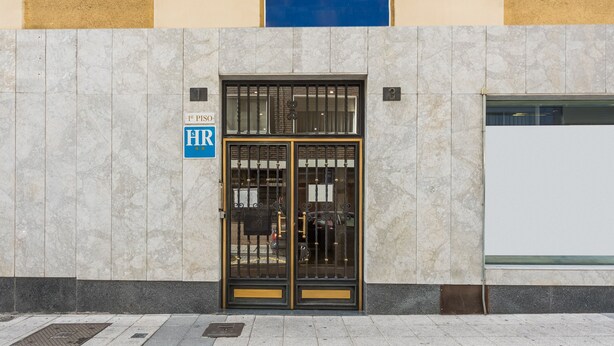 A building facade with a large glass door, a sign indicating '1st Piso' and 'HR', and a blue wall above. - Hostal Uria (Salamanca)