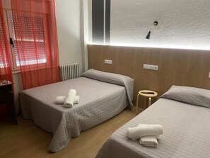 A hotel room with two beds, each with a quilted bedspread and rolled towels. There is a small wooden stool between the beds and a window with frosted glass. - Hostal Uria (Salamanca)