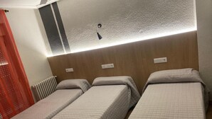 A hotel room with three single beds, a wooden headboard, a radiator, and a red curtain. - Hostal Uria (Salamanca)