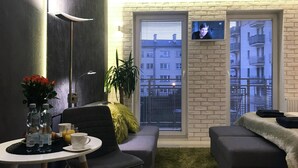 Un salon moderne avec un canapé, une petite table sur laquelle est posé un vase de fleurs, et un téléviseur fixé à un mur en briques.