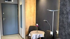 Une petite pièce moderne, avec une table ronde, deux chaises, un canapé, une lampe et une porte.