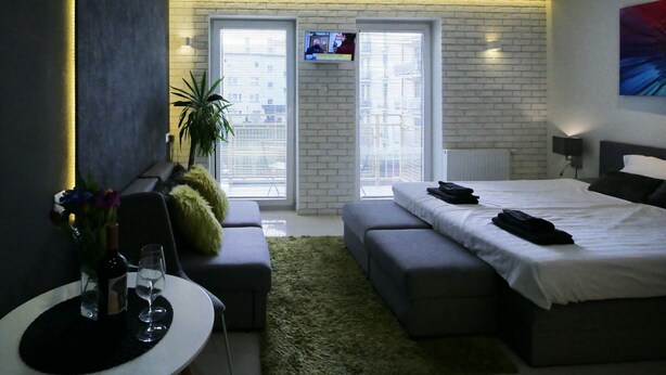 Une chambre moderne avec un grand lit, un coin salon avec une table et un téléviseur fixé au mur.