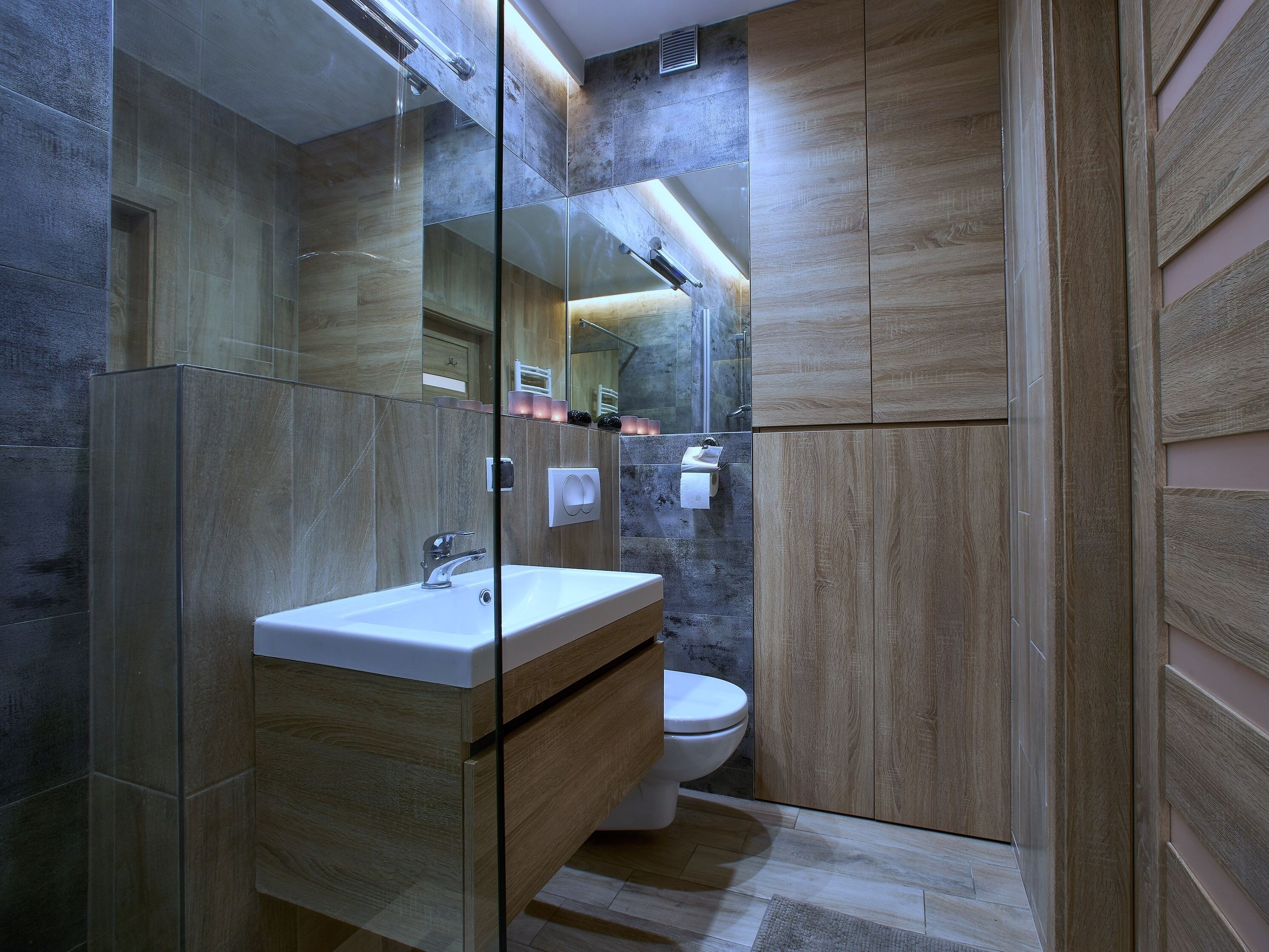 A modern bathroom with a glass-enclosed shower, a wooden vanity, and a toilet.