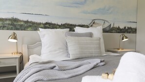 A neatly made bed with white and gray bedding, two bedside lamps, and a wall mural of a beach scene. - Havgaarden Badehotel (Vejby)
