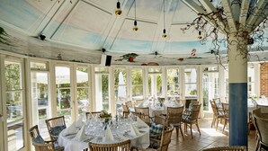 A dining area with round tables set for a meal, surrounded by wicker chairs with blue cushions. - Havgaarden Badehotel (Vejby)
